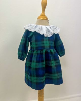 Čipkovaný biely golier dodáva šatám elegantný vzhľad, zatiaľ čo zelené káro prináša šmrnc tradície a nadčasového dizajnu....